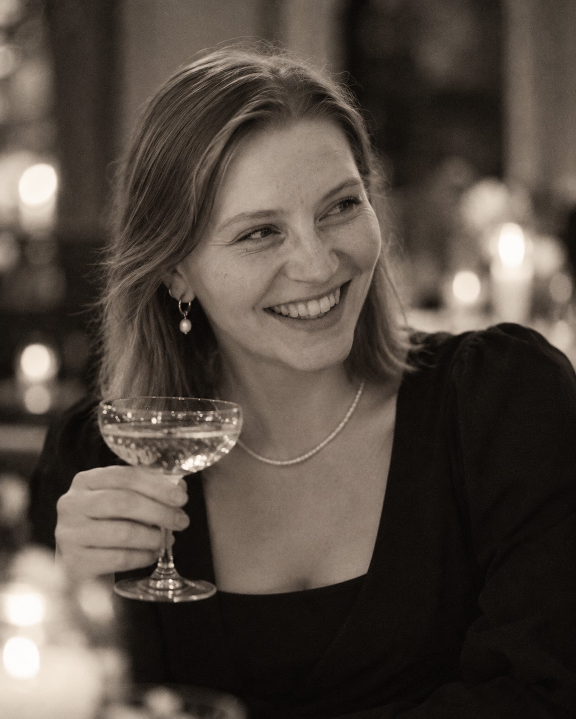 Maria lächelt mit einem Champagnerglas im Kerzenschein